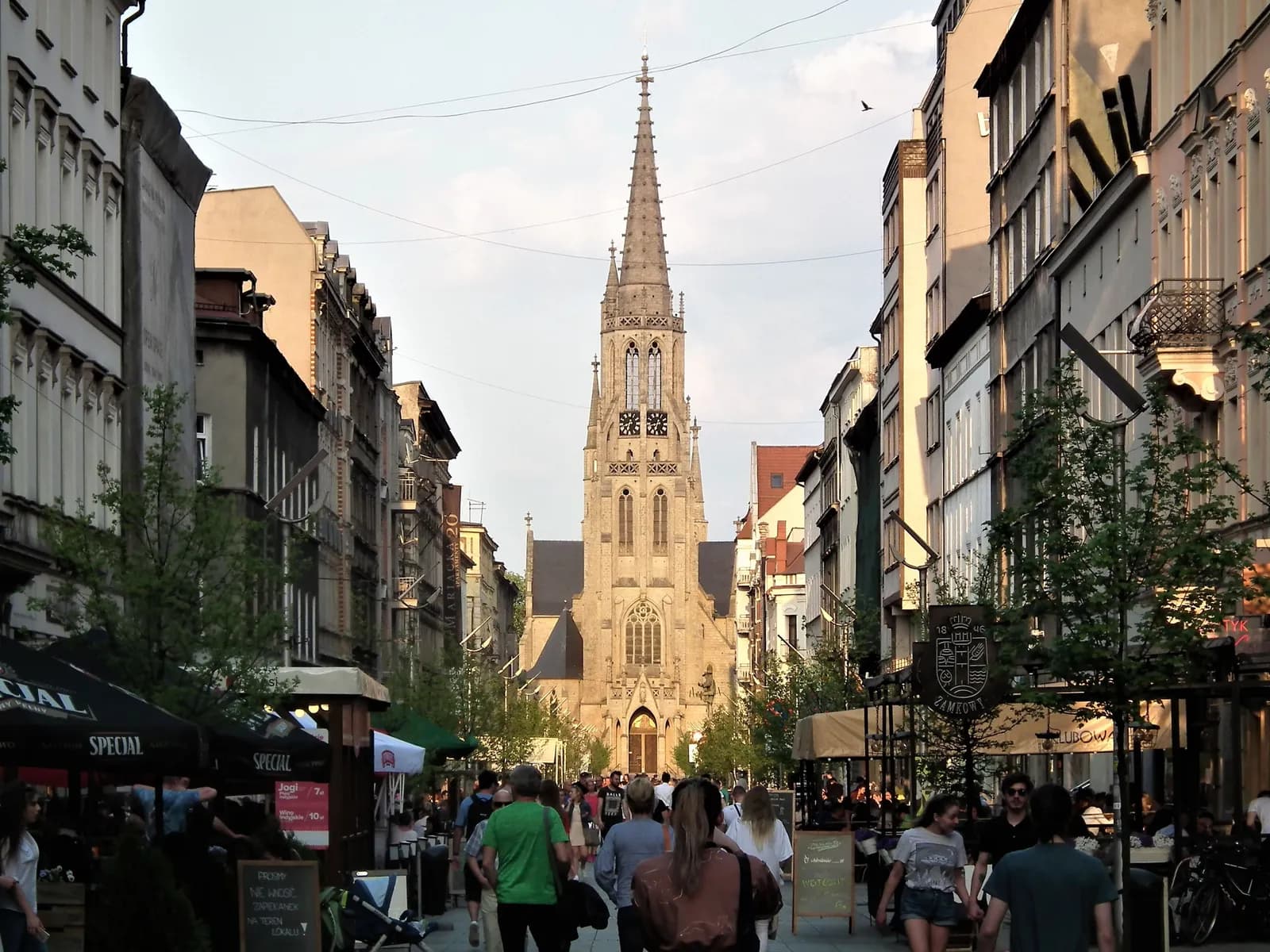 A long, narrow street stretches into the distance, lined with buildings on both sides, culminating in a tall, pointed cathedral steeple in the center.
